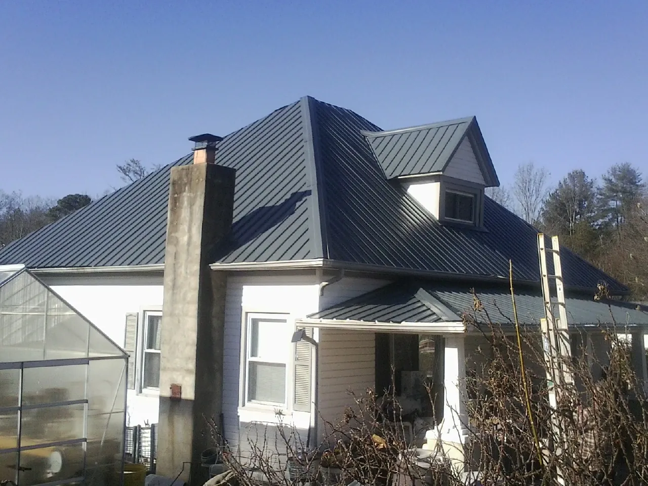 Dark blue standing seam metal roof on a white farmhouse with dormer — Slate & Tile Roof Repair by Roofing Brothers in Bokchito
