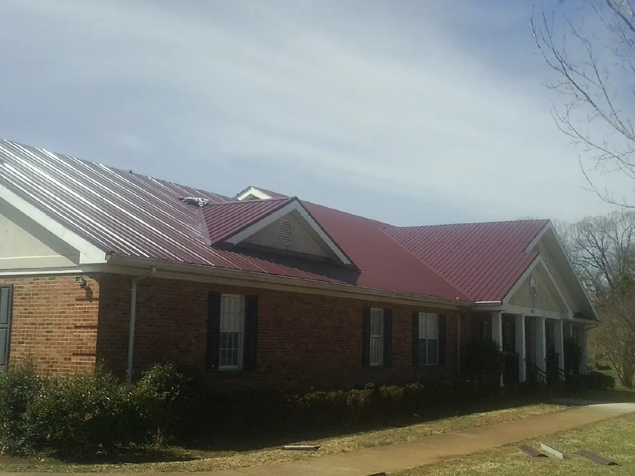 Red metal roof with gabled entries on a long brick building, from a Hail Damage Roof Repair job in Bokchito