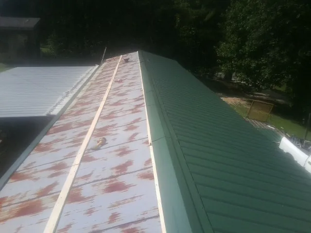 Old rusted panels beside newly installed green metal roofing — Wind Damage Roof Repair by Roofing Brothers in Bokchito