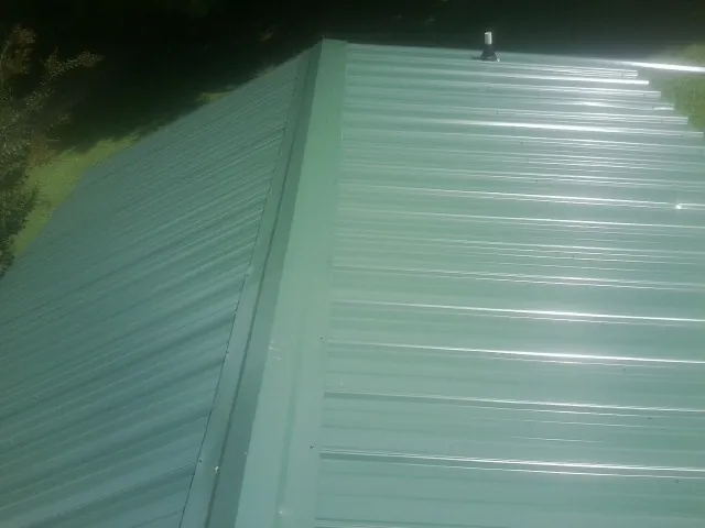 New green metal panels meeting at the ridge of a roof — Flat Roof Repair work by our crew in Bokchito