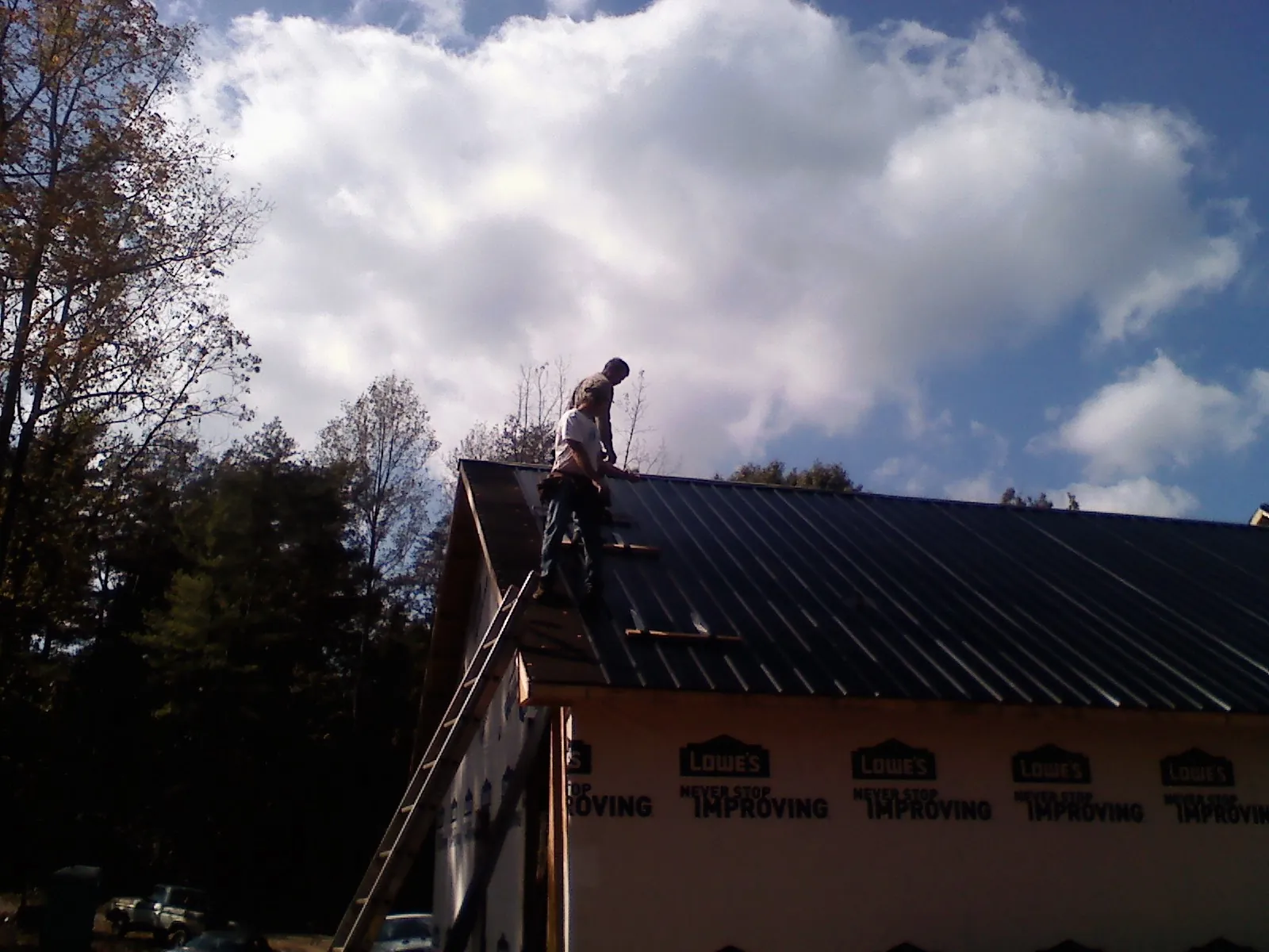 Roofer fastening dark metal panels high against a cloudy sky, from a Roof Inspection job in Bokchito