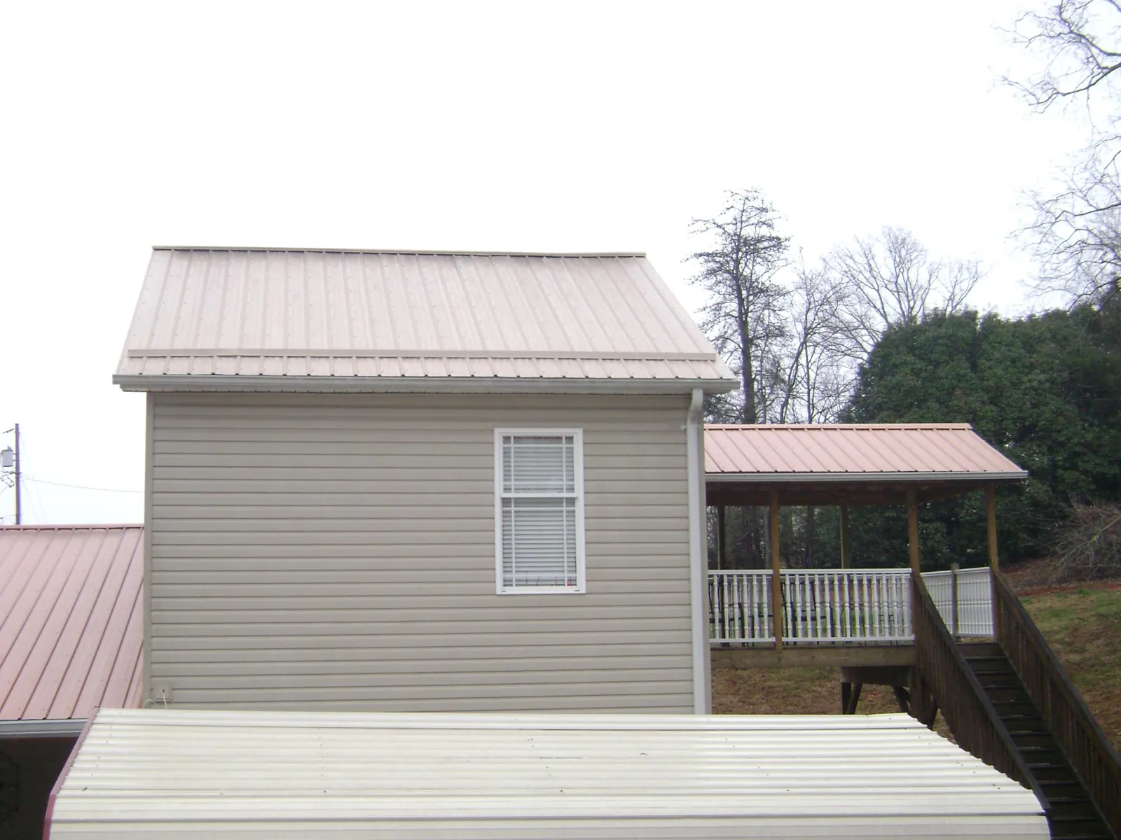 Tan metal roofs on a two story addition and attached porch, from a Roof Replacement job in Bokchito